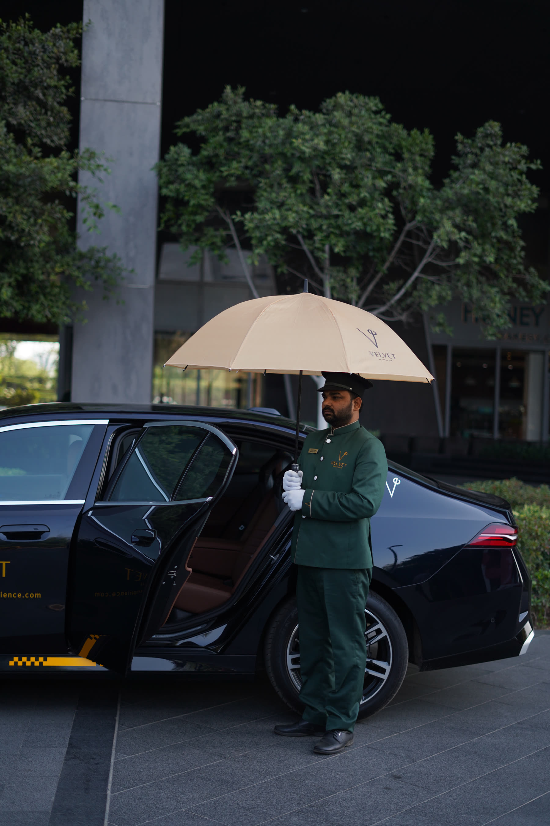 Velvet chauffeur holding umbrella by an open rear door